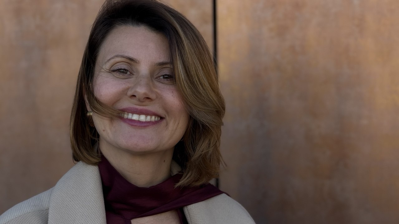 Екатерина Тельцова улыбается: портрет крупным планом, светлое пальто и бордовый шарф